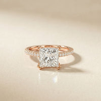 Rose gold ring with a large diamond and smaller diamonds on the band against a beige background Rose Gold