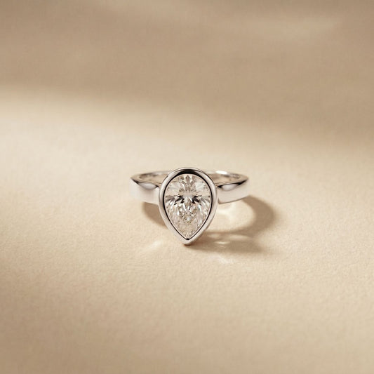 Diamond ring with a pear-shaped gemstone on a beige background