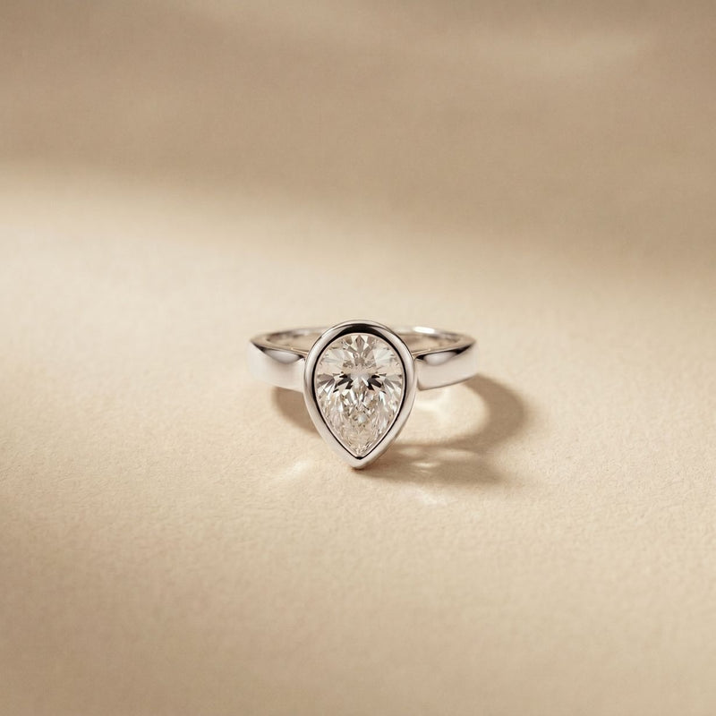 Diamond ring with a pear-shaped gemstone on a beige background White