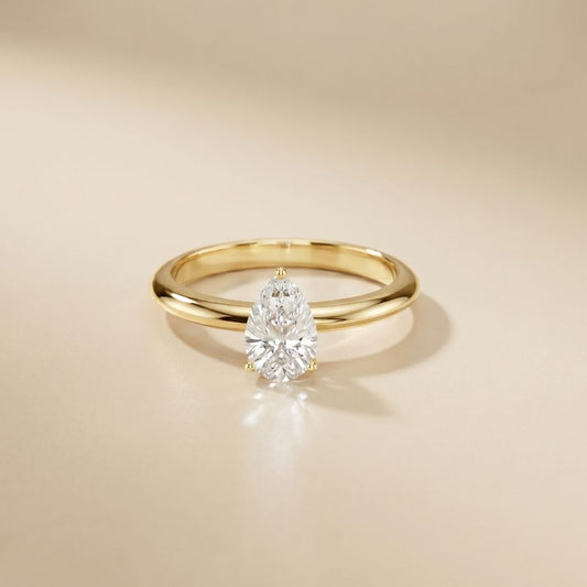 Gold ring with a pear-shaped diamond on a beige background