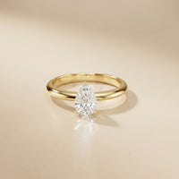 Gold ring with a pear-shaped diamond on a beige background Gold